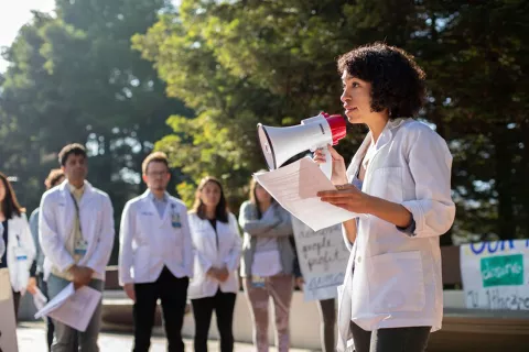 Sheyda Aboii, MS2, speaks to her fellow medical students, including, background left to right, Arun Burra, Andrés Calvillo and Avery Thompson and the community, at a White Coats for Black Lives (WC4BL) Teach-in, which set out to 'model an explicitly anti-racist healthcare education that elevates queer, disabled, formerly criminalized, and undocumented people of color in the communities and hospitals within which we work,' on the 4th anniversary of WC4BL, at a peaceful rally at the Parnassus campus